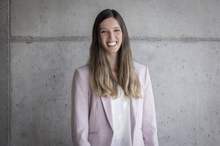 Ein Foto von der Frau Selina Wenk, Office Koordinatorin, vor einer grauen Wand.