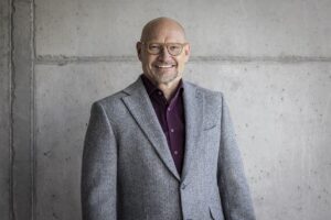 Ein Foto von dem Mann Hans Ebinger, Geschäftsführer von dem Switzerland Innovation Park Ost, vor einer grauen Wand.